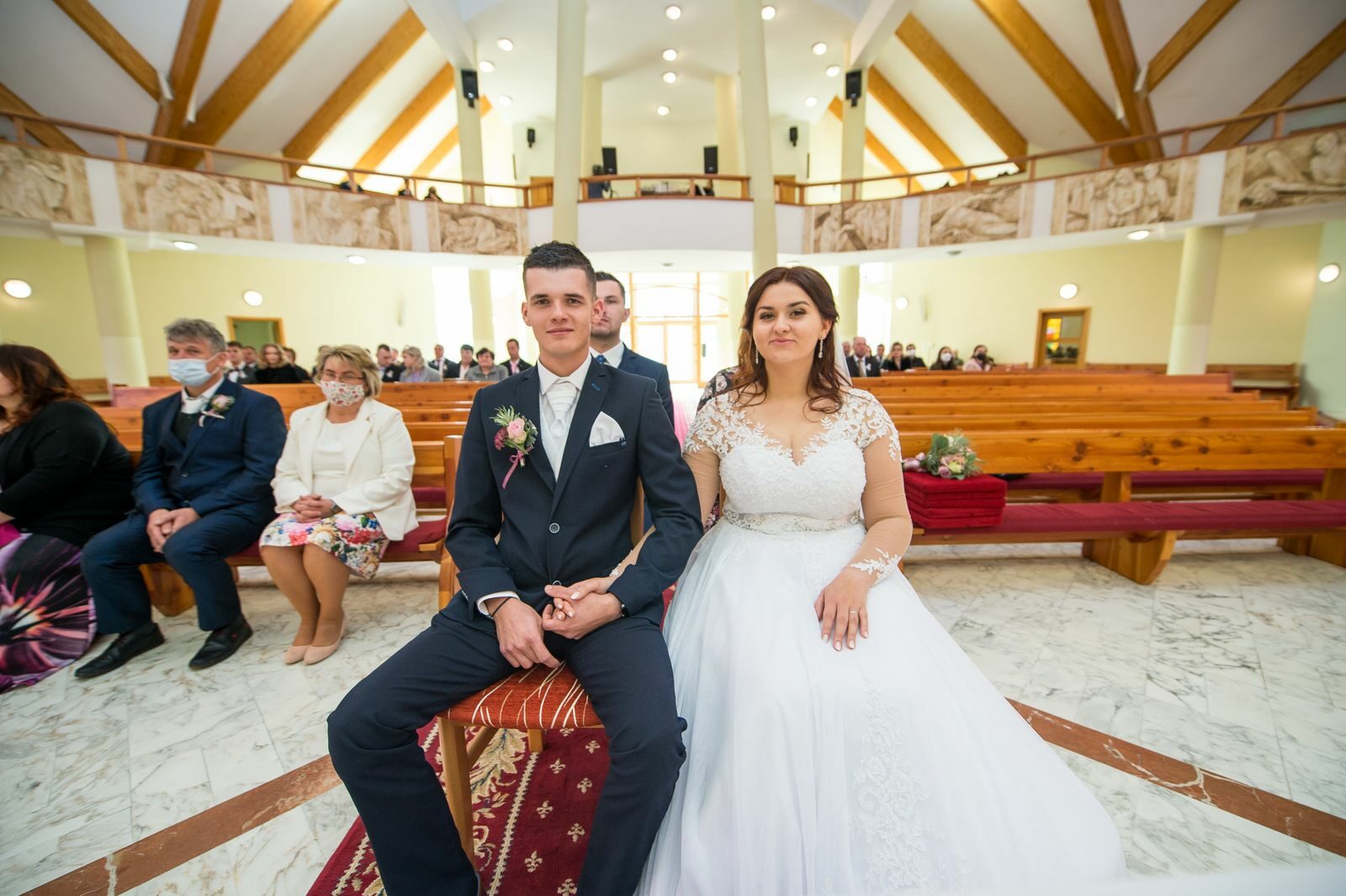 A bride and groom seated in a beautifully decorated church, surrounded by guests during their wedding ceremony.